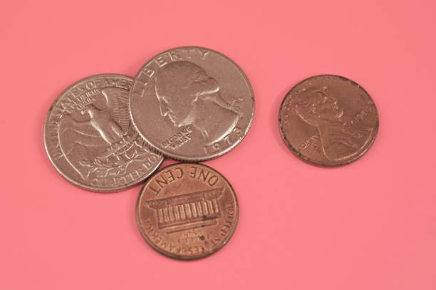 istock Two one-cent coins and two quarter dollar coins lying on a pink background. 1212810893