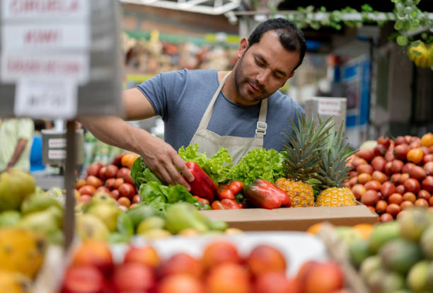 istock Handsome man working at a farmer's market adding products in a cardboard box 1212810952