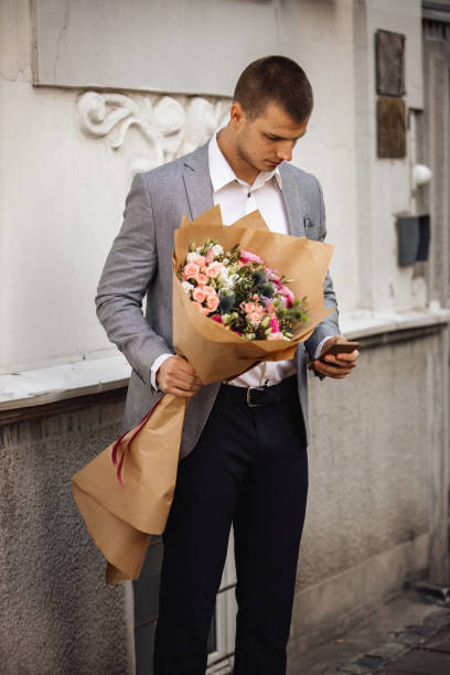 istock Young Man Holding Flower Bouquet And Text Messaging 1212818323