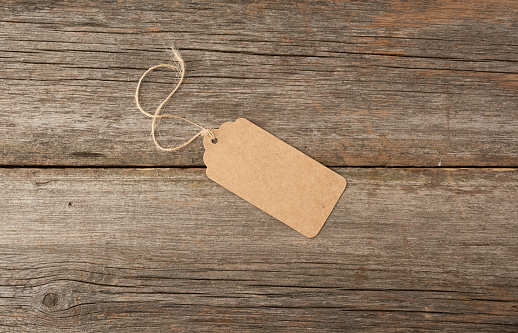 Empty brown paper tag tied with white string. Price, gift, sale tag on the gray wooden background, close up