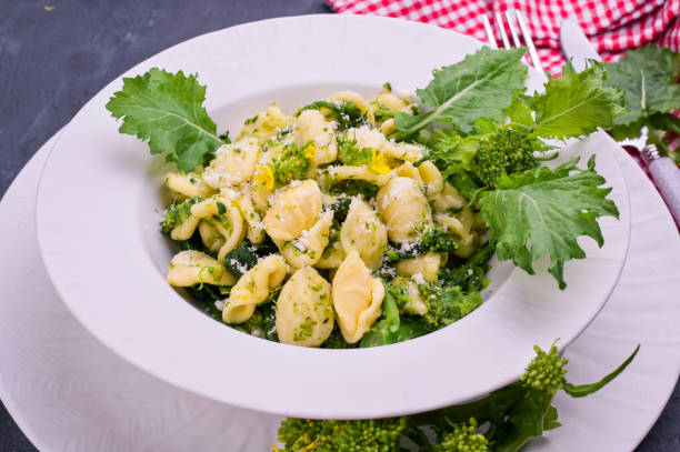 cime di rapa pasta in einem teller auf mit parmesan auf dem tisch. traditionelle sanierküche süditaliens, aus apulien. rustikale stil foto. kopierraum - orecchiette stock-fotos und bilder