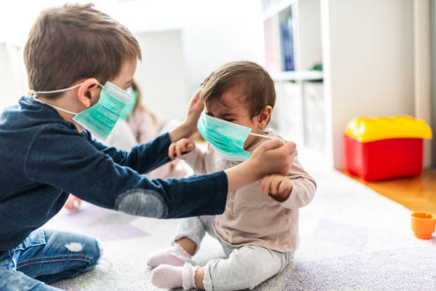kinder tragen verschmutzungsmasken zu hause - sibling baby three people baby girls stock-fotos und bilder