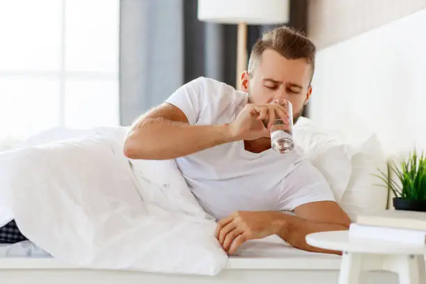 young healthy man drinking water in morning at window