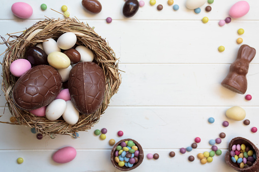 Top view of chocolate eggs on nest, chocolate rabbit and sweets on white wooden table with copy space
