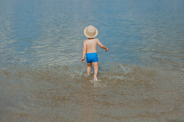 Cute little boy running through the water at the beach.