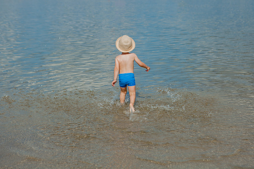 Cute little boy running through the water at the beach.