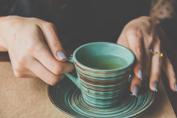 Las manos de las mujeres sostienen una taza de cerámica verde con un patrón creativo de estilo japonés - foto de stock