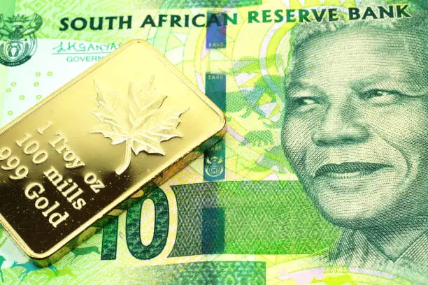 Photo of A green ten rand note from South Africa with a gold coin in macro