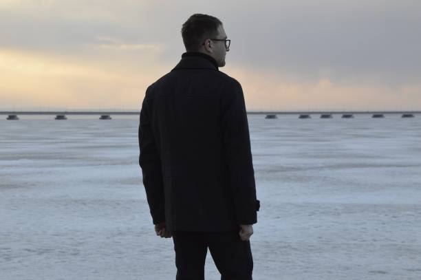 giovane russo in cappotto che guarda il mare giapponese ghiacciato in una serata primaverile - russian ethnicity cold relaxation nature foto e immagini stock
