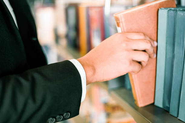 Business man or student holding a book on hand or Picking a book on bookshelf in the library bookshelves background - Business Education Study Concept