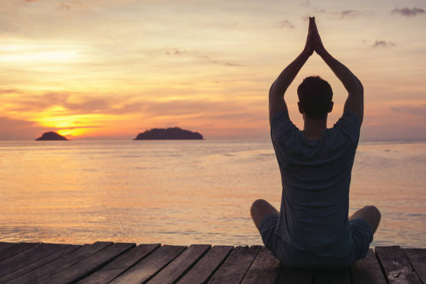 yoga zen e meditazione, silhouette dell'uomo seduto sul molo al tramonto - equanimity foto e immagini stock