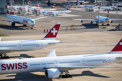 Zurich, Switzerland - March 16, 2020: Overview of Zurich Airport with Swiss International Air Lines airplanes parked on remote stands. Lufthansa subsidiary Swiss International Air Lines is taking half its fleet out of service and reducing working hours for flight personnel to help safeguard its finances during the coronavirus outbreak.