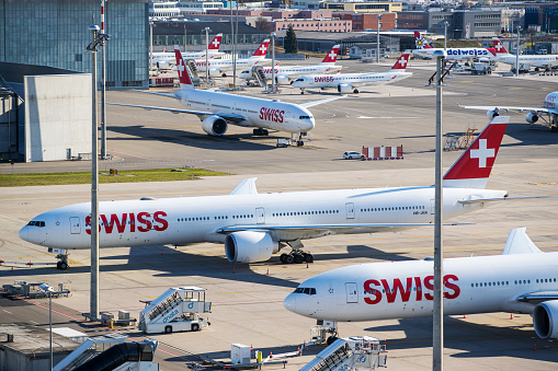 Zurich, Switzerland - March 16, 2020: Overview of Zurich Airport with Swiss International Air Lines airplanes parked on remote stands. Lufthansa subsidiary Swiss International Air Lines is taking half its fleet out of service and reducing working hours for flight personnel to help safeguard its finances during the coronavirus outbreak.