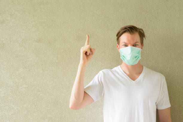 istock Young man pointing up and wearing mask for protection from corona virus outbreak 1212882369