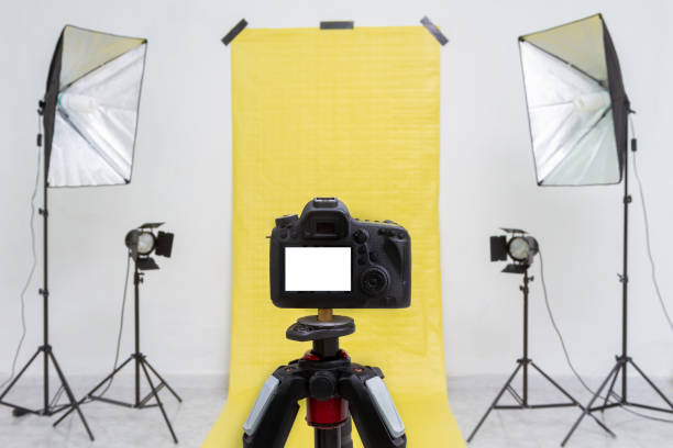 istock Camera in a photo studio with yellow backdrop and light equipment. White screen mockup 1212885890
