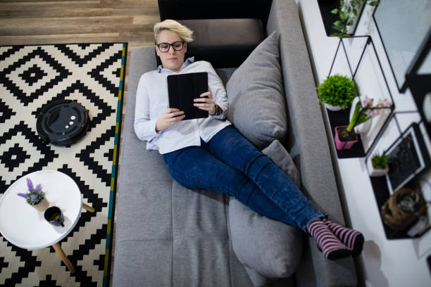 istock Robotic vacuum cleaner cleaning the room while woman relaxing on sofa. 1212886897