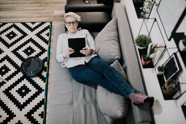 istock Robotic vacuum cleaner cleaning the room while woman relaxing on sofa. 1212887456