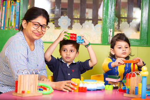 Teacher teaching toy activity to preschool children, looking at the camera