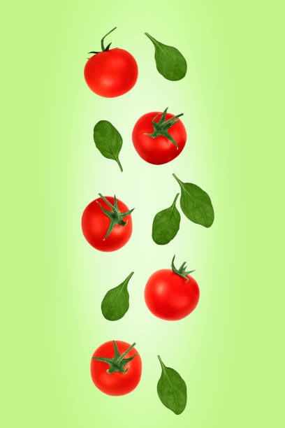 istock Falling red cherry tomatoes and spinach leaves isolated on a green background, clipping path. Flying food. 1212894866