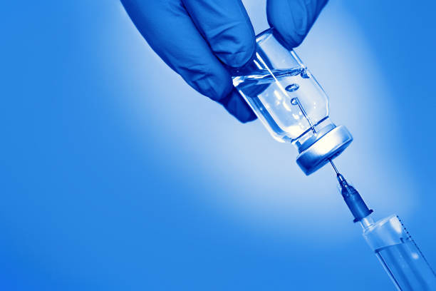 вакцина в бутылке со шприцем на синем фоне. концепция медицины, здравоохранения и науки - syringe vaccination human hand medical procedure стоковые фото и изображения