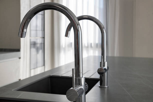 istock Modern square kitchen sinks and polished chrome faucets installed on a dark grey granite kitchen island 1212896241