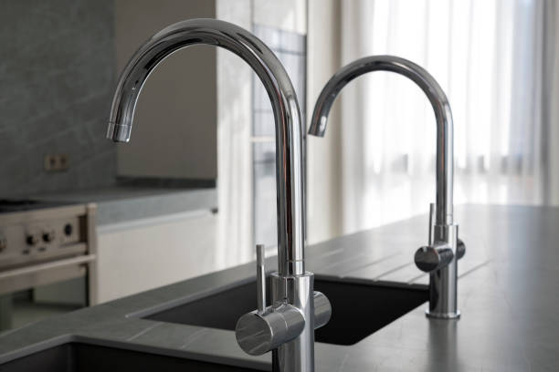 istock Modern square kitchen sinks and polished chrome faucets installed on a dark grey granite kitchen island 1212896277