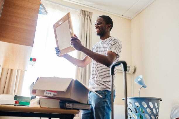 This is going up on the wall Cropped shot of a cheerful young man unpacking his stuff after arriving at his new home inside during the day dorm room photos stock pictures, royalty-free photos & images