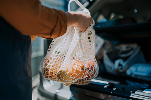 una repartidora asiática china recibiendo los comestibles y frutas de su cliente ordenden compras en línea en bolsas de reciclaje de su maletero del coche y entregarlo a su cliente photo
