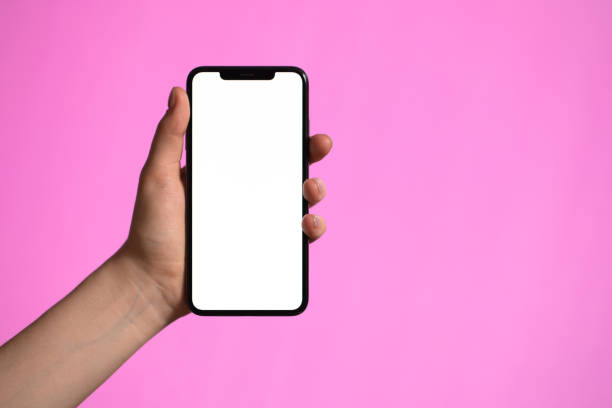 istock Close up of female hands using smartphone with white screen mobile phone for graphic display montage on a pink background 1212907334
