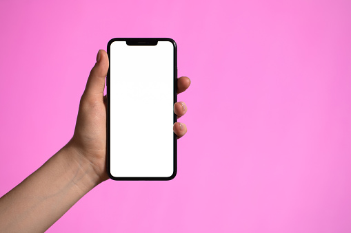 Close up of female hands using smartphone with white screen mobile phone for graphic display montage on a pink background