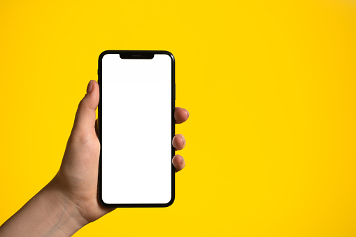 Hand holding mobile phone with blank white full screen on a yellow background