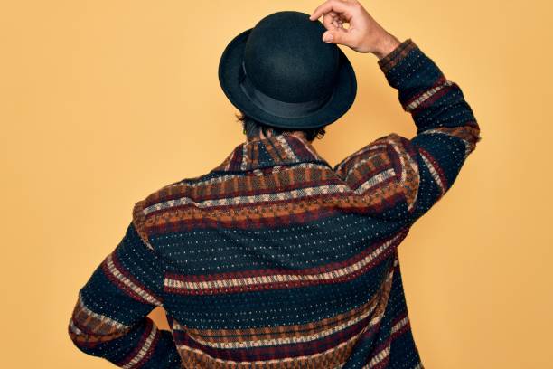 Young handsome hispanic bohemian man wearing hippie style and boho hat Backwards thinking about doubt with hand on head