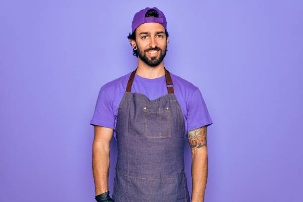 Young handsome hispanic man with bear wearing professional apron working as tattoo artist with a happy and cool smile on face. Lucky person. Young handsome hispanic man with bear wearing professional apron working as tattoo artist with a happy and cool smile on face. Lucky person. in pride we trust stock pictures, royalty-free photos & images