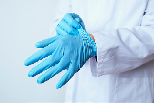 closeup of a caucasian doctor man, wearing a white coat, putting on a pair of blue surgical gloves
