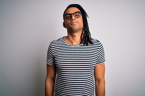 Young handsome african american man with dreadlocks wearing striped t-shirt and glasses Relaxed with serious expression on face. Simple and natural looking at the camera.