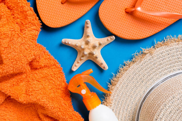 istock Summer beach flat lay accessories. Sunscreen bottle cream, straw hat, flip flops, towel and seashells on colored Background. Travel holiday concept with copy space 1212920818