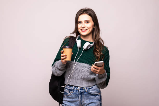 istock Young beautiful woman with backpack holding coffee using smart phone isolated on white background 1212921422