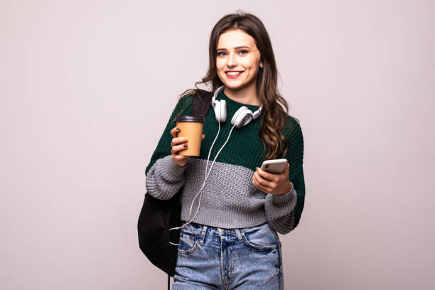 istock Young beautiful woman with backpack holding coffee using smart phone isolated on white background 1212921462