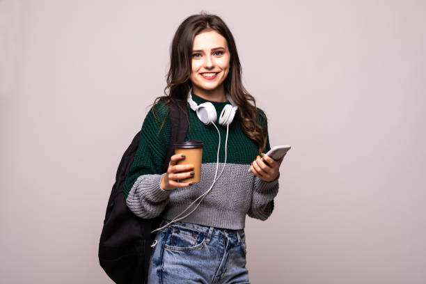 istock Young beautiful woman with backpack holding coffee using smart phone isolated on white background 1212921527