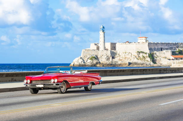 American red 1959 convertible vintage car on the promenade Malecon and in the background the Castillo de los Tres Reyes del Morro in Havana City Cuba - Serie Cuba Reportage stock photo