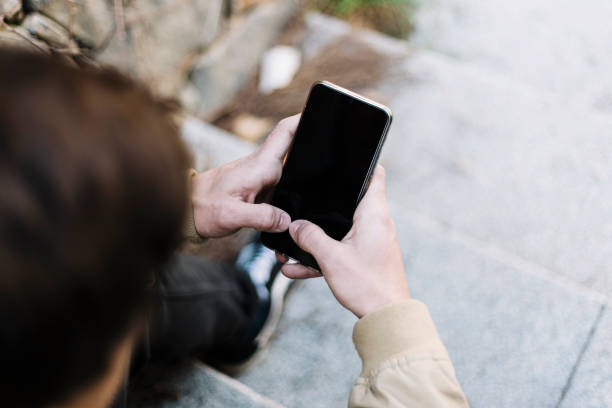 istock Rear view of young man using mobile phone while sitting outdoors 1212925480