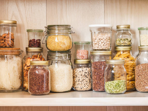 estante en la cocina con varios cereales y semillas - guisantes split, semillas de girasol y calabaza, frijoles, arroz, pasta, avena, cuscús, lentejas, bulgur en frascos de vidrio - comida básica fotografías e imágenes de stock