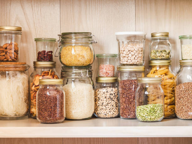 Shelf in the kitchen with various cereals and seeds - peas split, sunflower and pumpkin seeds, beans, rice, pasta, oatmeal, couscous, lentils, bulgur in glass jars stock photo