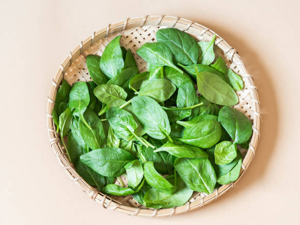istock Wooden wicker tray with fresh spinach on a light background. Top view. 1212928624
