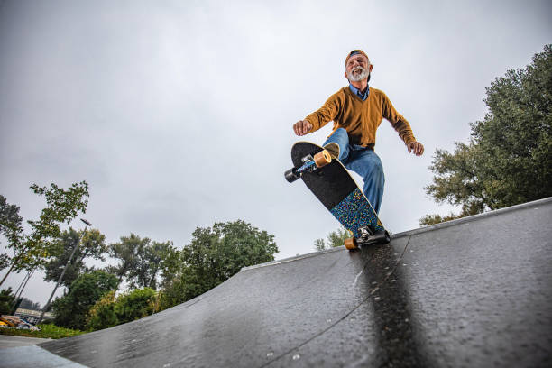 au-dessous de la vue de l’homme aîné heureux faisant du skateboard sur une rampe au stationnement. - skateboard park ramp park skateboard photos et images de collection