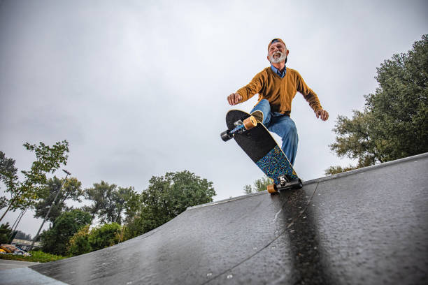 ниже вид счастливого старшего человека скейтбординга на рампе в парке. - skateboard park ramp park skateboard стоковые фото и изображения