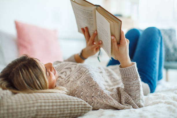 istock Young woman lies on her back in bed reading a book 1212930397