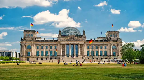 German flags waving in the wind at famous Reichstag building, seat of the German Parliament Deutscher Bundestag , on a sunny day with blue sky and clouds, central Berlin Mitte district, Germany