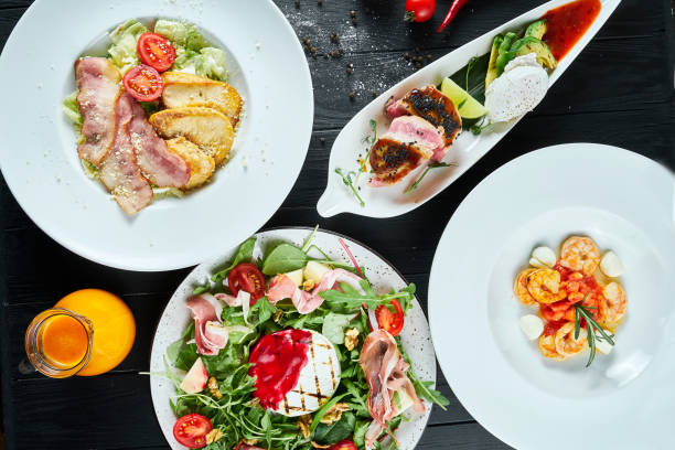 istock Dinner table with different dishes - Caesar salad, tuna steak, shrimp soup, grilled camembert salad 1212939768