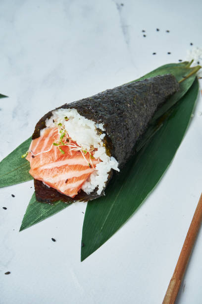 close up view on fresh, seafood temaki sushi with salmon on white background. traditional hand roll. vertical, selective focus - handroll imagens e fotografias de stock